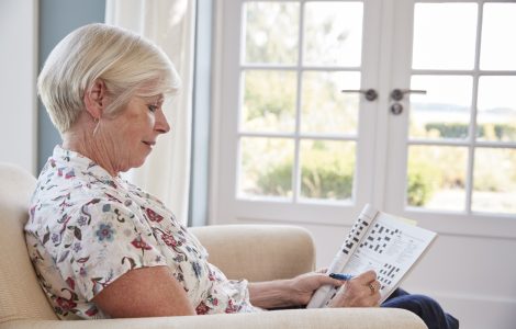 Senior woman sitting in armchair doing  a crossword at home