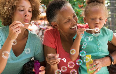 Black multi-generation family blowing bubbles outdoors
